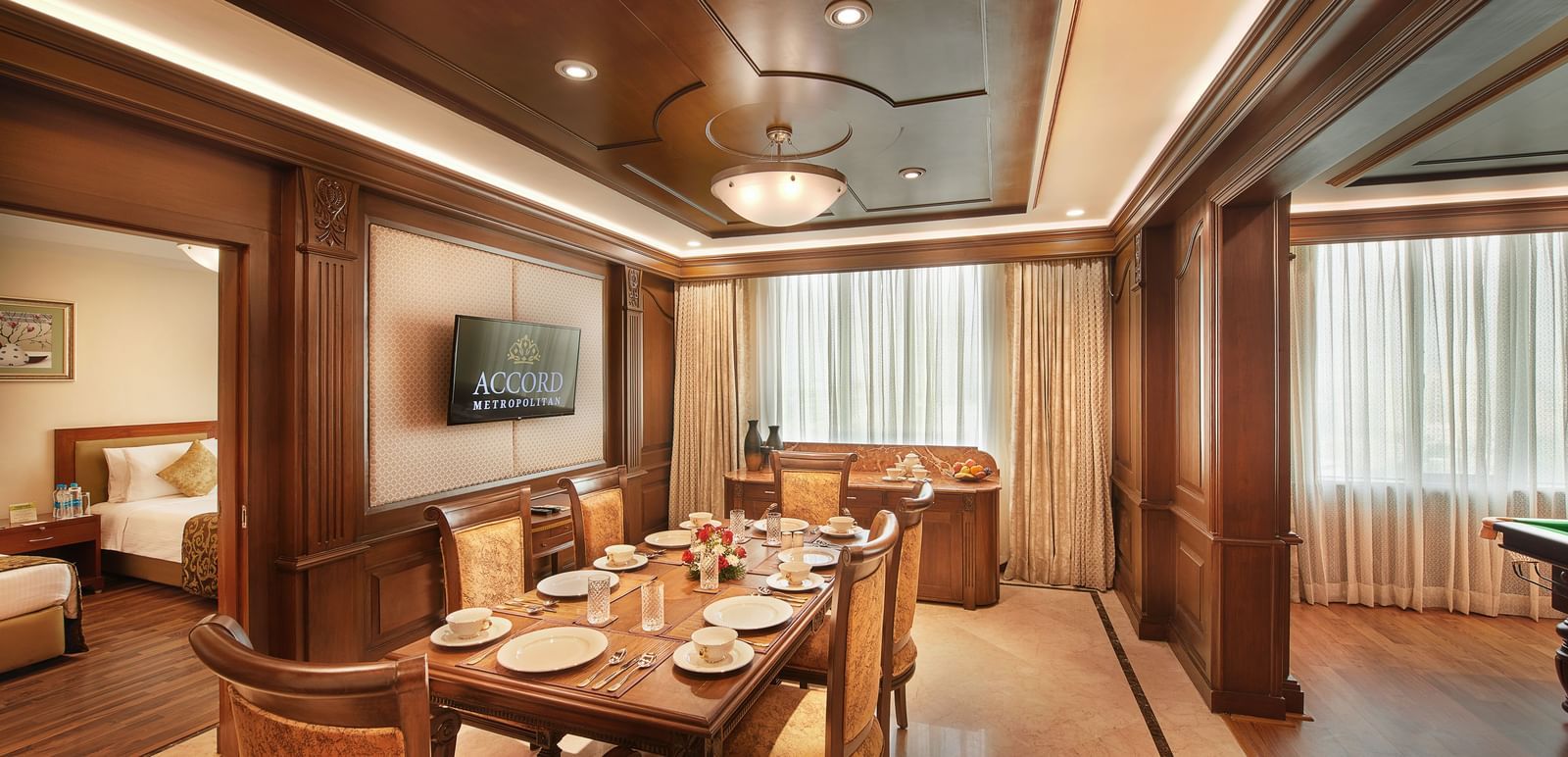 An image of a wooden furnished dining room with chairs and table, and an attached bedroom - Accord Hotels and Resorts